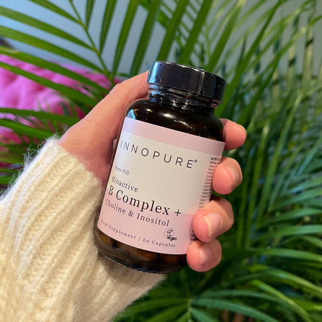 Hand holding a bottle of Innopure Bioactive B Complex supplement with plants in the background