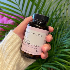Hand holding a bottle of Innopure Bioactive B Complex supplement with plants in the background