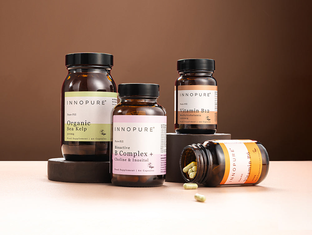 Four Innopure supplement jars: Organic Sea Kelp, Bioactive B Complex + Choline & Inositol, Vitamin B12, and Vitamin B6 tipped over with capsules spilling out